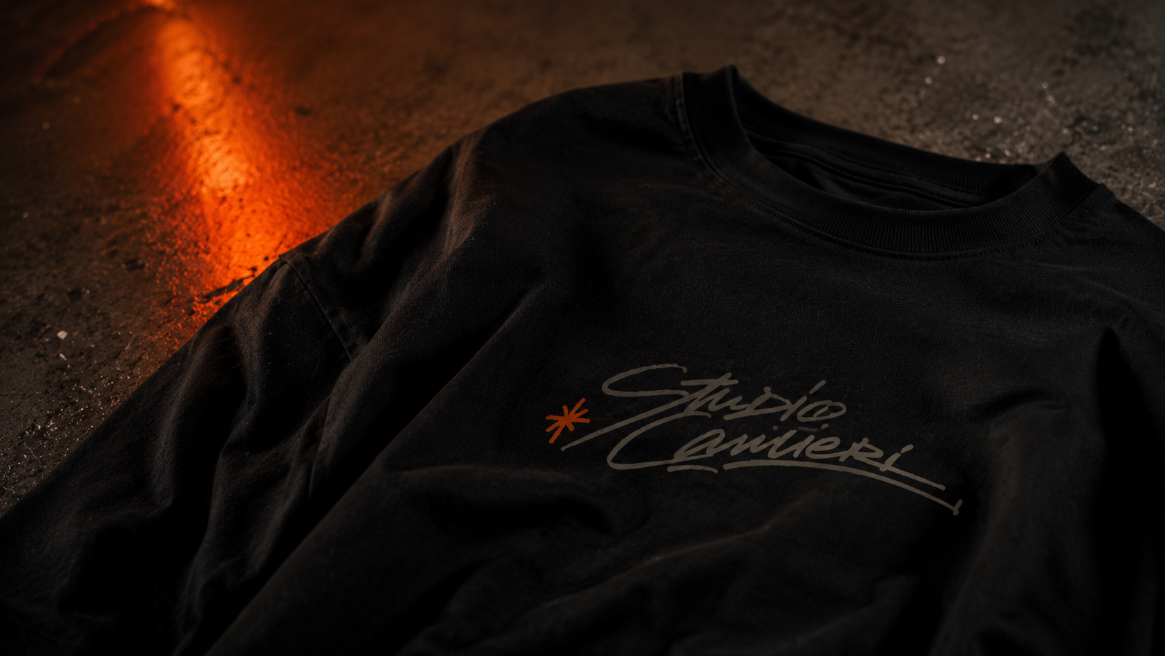 Camiseta preta com a assinatura do Studio Cantieri sobre o asfalto, reflexo de luz laranja